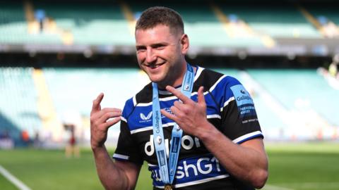 Finn Russell holding his hands up while standing on the pitch with a Premiership winner's medal around his neck