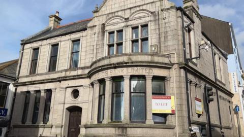 The building which says "Lloyd's Bank Limited" on it. There is a sign which says "Charterwood, to let" on it. 