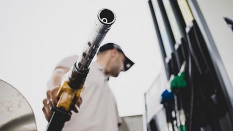 A low-angle picture of a man holding a fuel pump at a petrol station