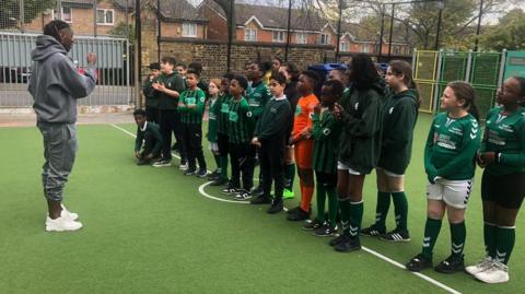 Eberechi Eze stands in front of pupils during a sports lesson at school 