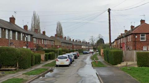 A residential street with cars parked on one side of the road.