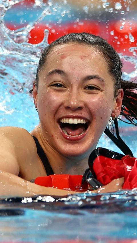 Alice Tai is in a swimming pool with water splashing around her. She is grining widely and has black hair tied back in a ponytail.