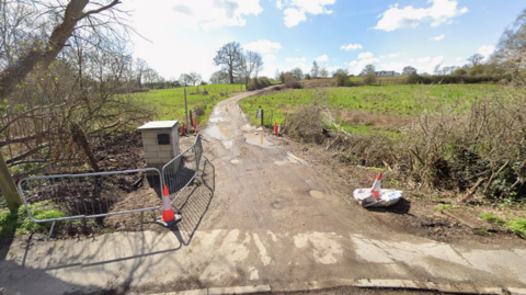 A Google maps image of the entrance to a field. There is a hard-standing road going through the field, leading to caravans far in the background.