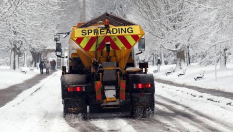 A council gritter spreads grit on snowy winter roads.