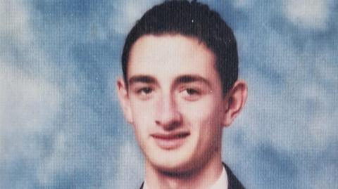 School photo of Gavin Brett looking into the camera with slight smile against a blue and white background