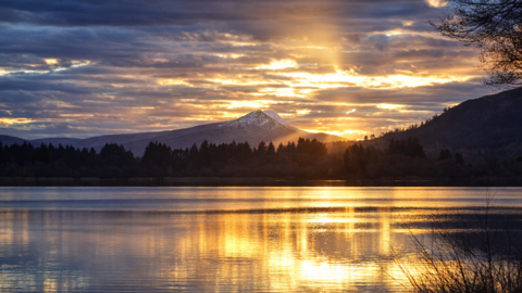 A snow-capped Ben Lomond in the distance, with Lake Menteith in the foreground, the sun is reflected on the rippled water.