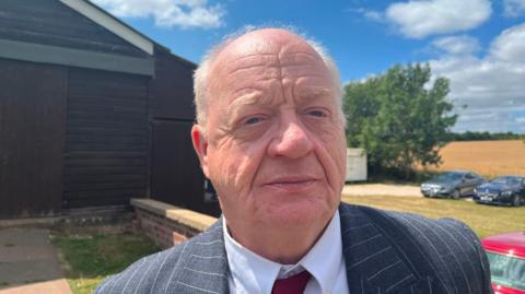 A head and shoulders image of an older man in a grey suit and tie