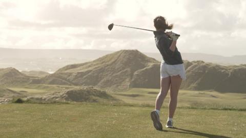 A girl tees off at golf
