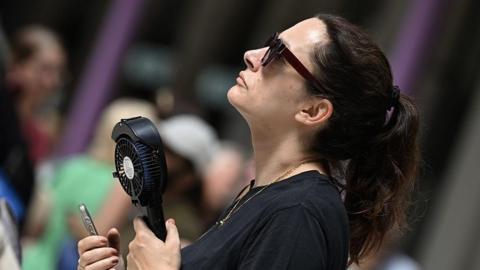 A woman wearing a black top holding a black handheld electric fan.