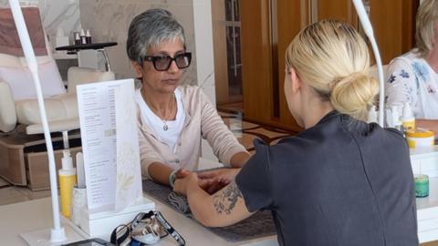 Sindy Sidhu sits at a spa with her hands on a table as they are massaged by a therapist