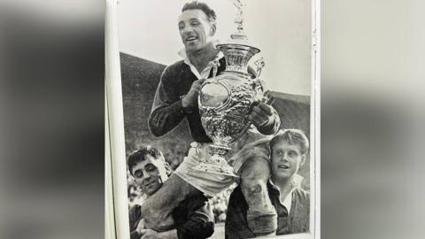 A black-and-white framed photo of two Workington Town players lifting another player holding the Challenge cup.