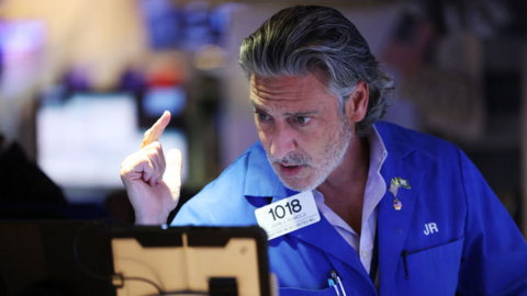 US stock market trader with grey hair and beard, wearing blue trading jacket with numbered badge