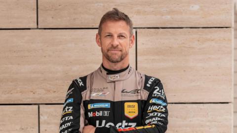 Jenson Button pictured in a racing uniform, with his arms folded