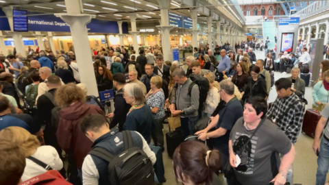 A crowd of people at London St Pancras station in London. They're carrying rucksacks or suitcases as they wait to go through departures and board a Eurostar train across the Channel.