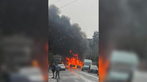 Two cars on fire in a rainy street.