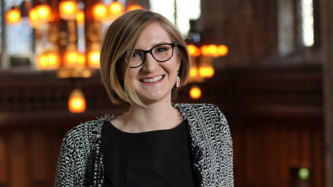 Woman with blonde hair and glasses, blurry lights in the background