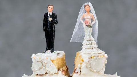 A wedding cake cut down the middle, splitting the bride and groom