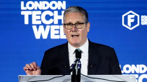 Starmer gestures as he speaks at a lectern in front of a blue background reading "london tech week".