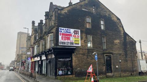 View of Westgate in Bradford, showing a three-story end-terrace building with a political campaign office on the ground floor.