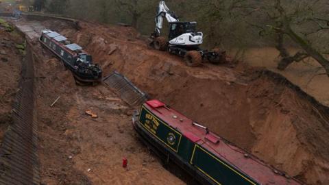 Two narrowboats being pulled clear from an empty canal ditch 