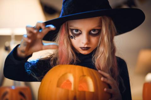 a girl dressed as a witch next to a carved pumpkin