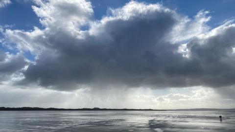 A huge blue/grey cloud over the sea with sunlight behind it