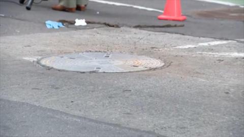 A covered manhole on a street with an orange cone nearby 