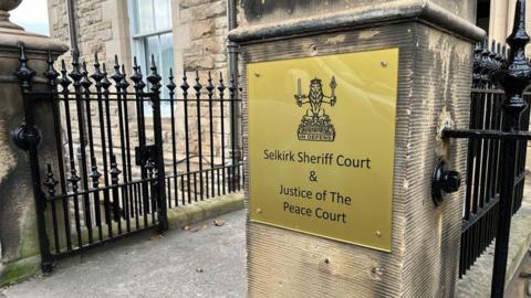 The outside of Selkirk Sheriff Court with a sign on a stone gatepost and black railings leading up to the court