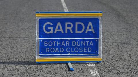 A blue Garda road closed sign sits in the middle of a road.