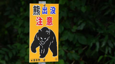 Close-up of a yellow sign warning of bear sightings in Japan, showing a drawing of a menacing black bear