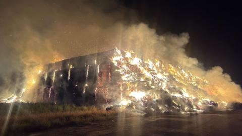 A large stack of hay bales on fire in the middle of the night. 