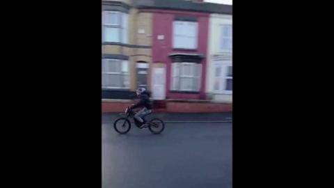 Boy on e-bike in police pursuit down street with terraced houses.