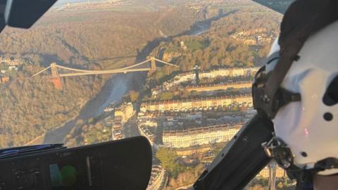 A photo taken over the shoulder of a pilot looking over the Clifton Suspension Bridge in Bristol in the sunshine.