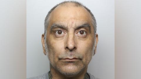 A custody photo featuring a man with large brown eyes and grey eyebrows, with short grey receding hair.