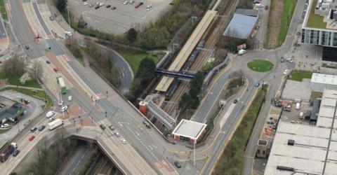 An aerial view of Salford Crescent station, showing a train at one of its platforms, which runs beneath a dual carriageway