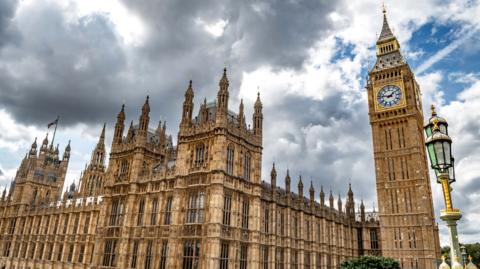 The House of Parliament and the Big Ben - the building and clocktower as viewed from Westminster Bridge against a grey clouded sky.