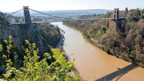 The Clifton Suspension Bridge seen from above over the River Avon. Bristol can be seen in the distance.