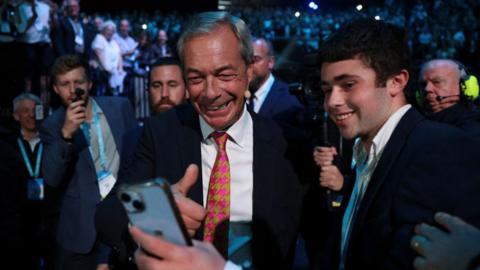 Nigel Farage getting a photo with a fan at Reform UK's conference in Birmingham