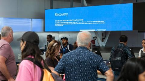 A man at JFK airport looks at a blue screen on a crashed Windows screen