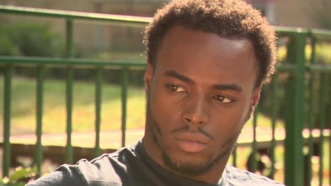 Jamar Powell, a young black man, looks away from the camera. He has short hair and a beard and is standing in front of a green fence.