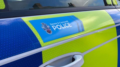 Devon and Cornwall Police logo on the side of a police vehicle. The car is blue and yellow.