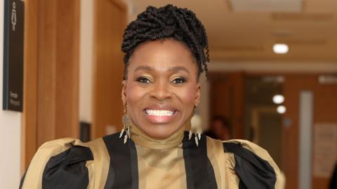 Mae Rakie Ayola n gwenu ar y camera 