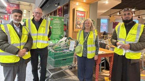 Three men and a a woman wearing hi-vis jackets stand outside a Morrisons supermarket