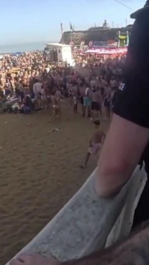 A large group of people on a beach with police overlooking.