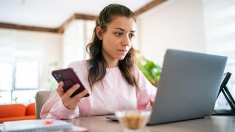 A woman checking her laptop and phone inside at home