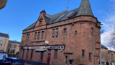 An old redbrick building with a black roof and worn sign 