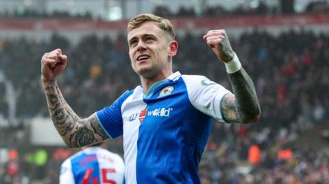 Sammie Szmodics, wearing Blackburn's blue and white kit, raises his arms - which are covered in tattoos - and clenches his fists after scoring a goal