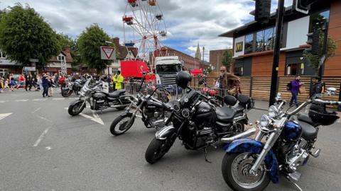 A row of motorbikes parked in front of a McDonald's branch on the right and a ferris wheel in the background.