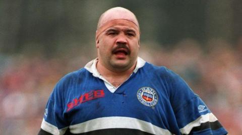 Gareth Chilcott in his rugby uniform in 1993. He has a headband around his head and a mustache.