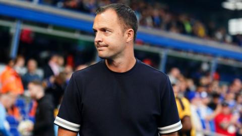 chris davies looks to the side and wears a navy t shirt